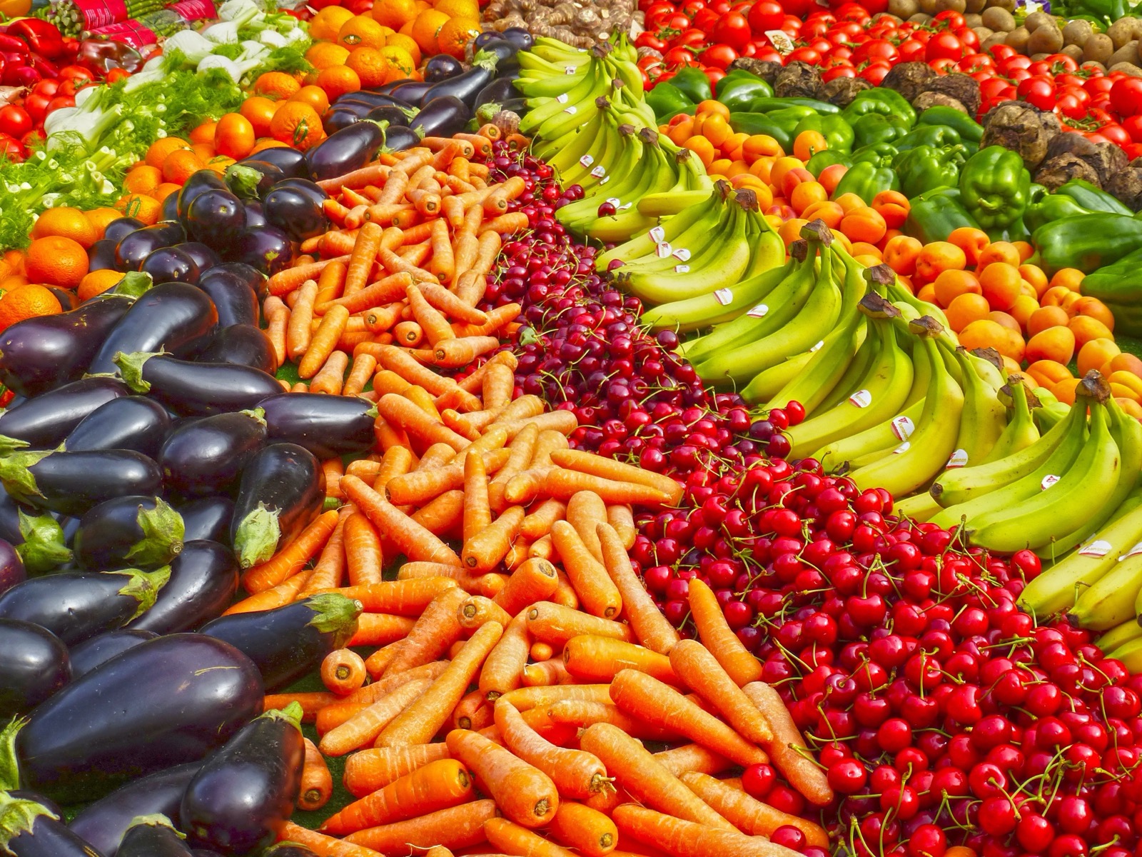 A colorful overhead display of fresh vegetables and fruits including carrots, eggplants, cherries and bananas at a market