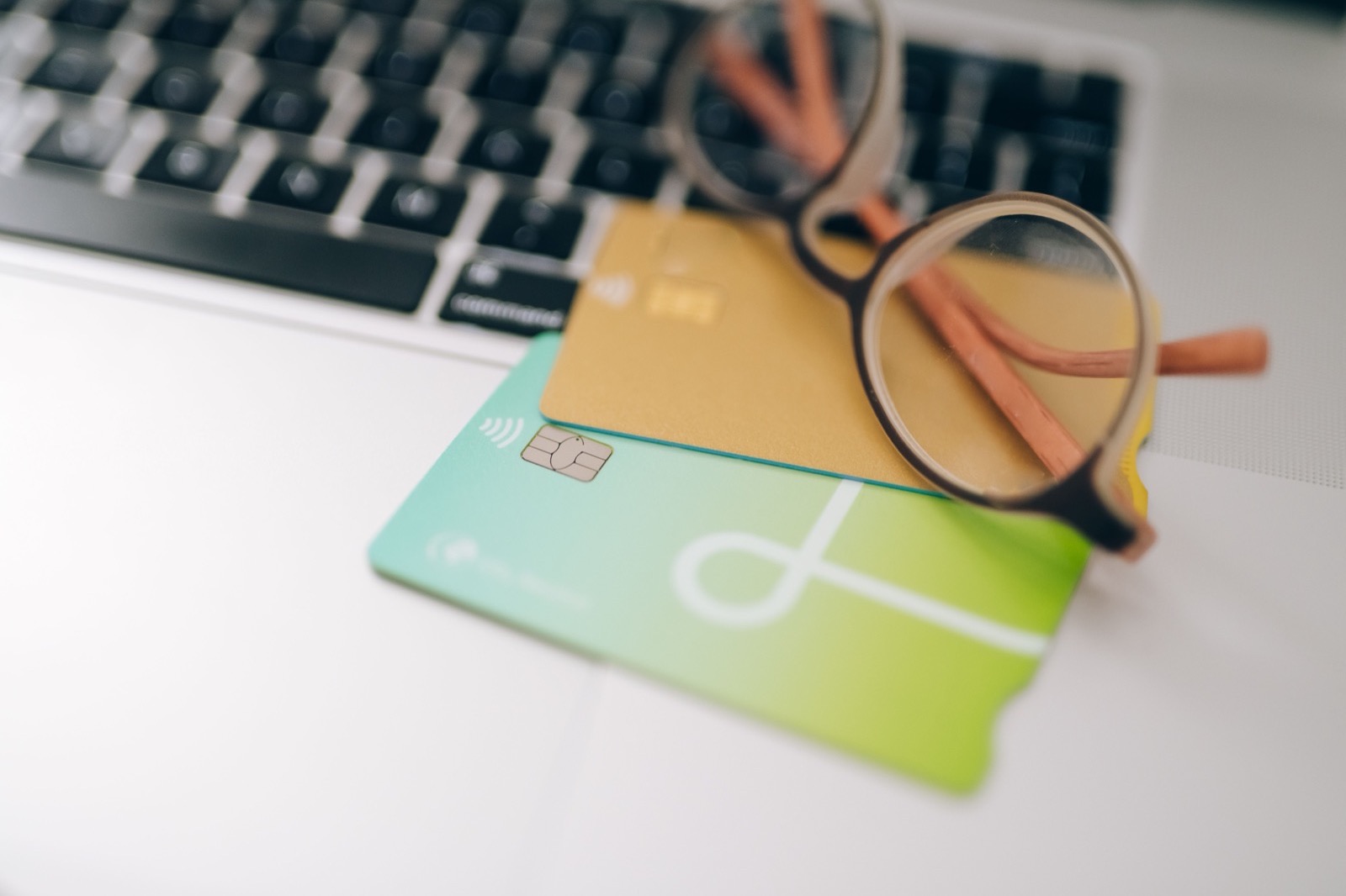 Two brand-neutral bank cards and a pair of glasses resting on a laptop keyboard