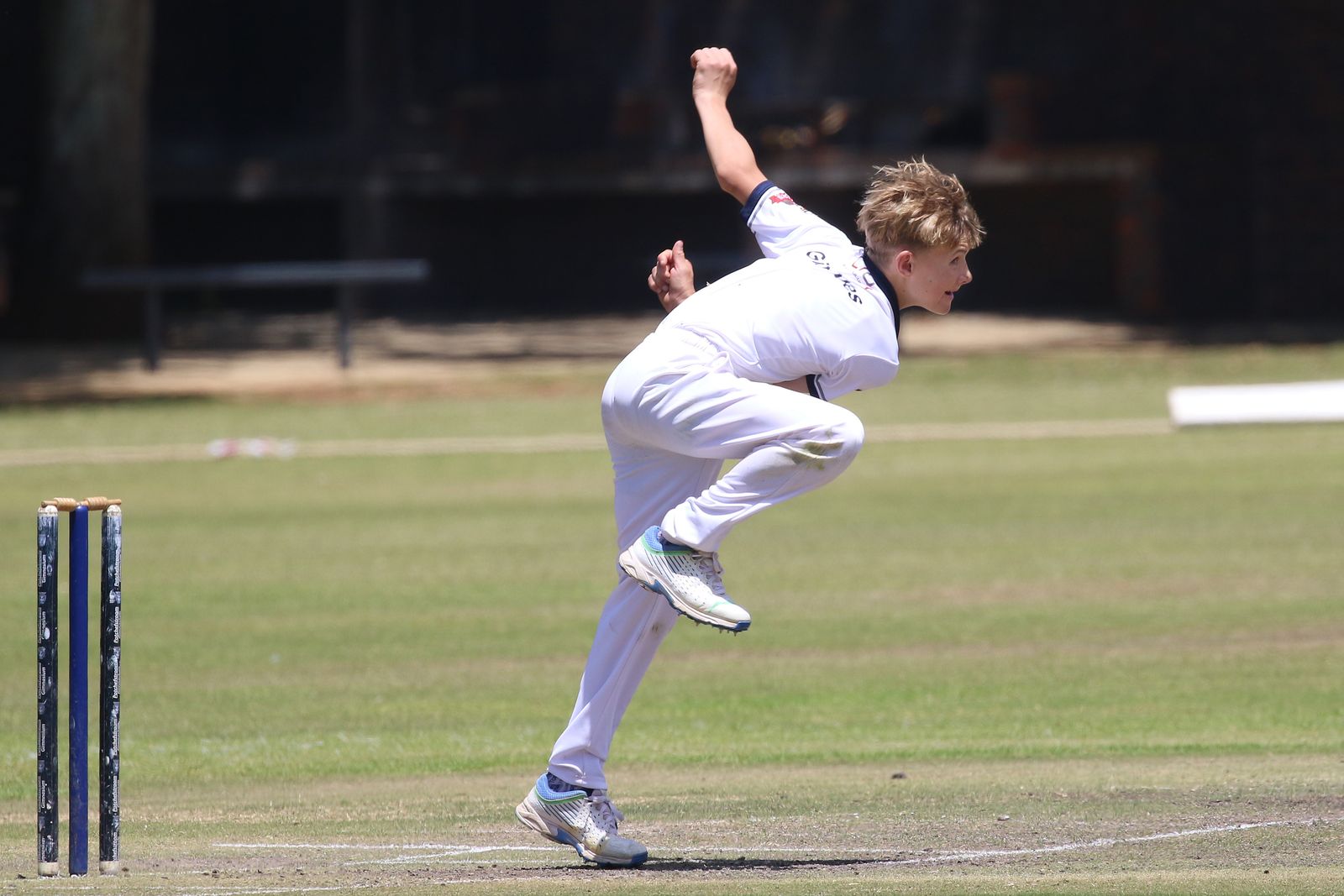 A cricketer in delivery stride, mid-bowling action, on a grass ground